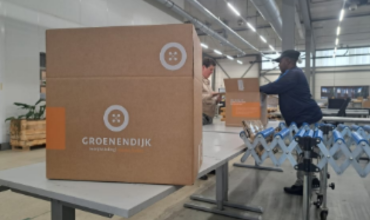 Een medewerker van Ferm Werk pakt een doos uit met het logo van Groenendijk Bedrijfskleding erop.
