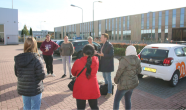 Een groep mensen staat op de parkeerplaats bij het kantoor van Ferm Werk.
